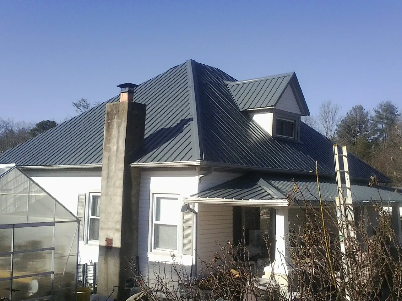 Dark blue standing seam metal roof on a white farmhouse with dormer — Slate & Tile Roof Repair by Roofing Brothers in Buffalo Grove