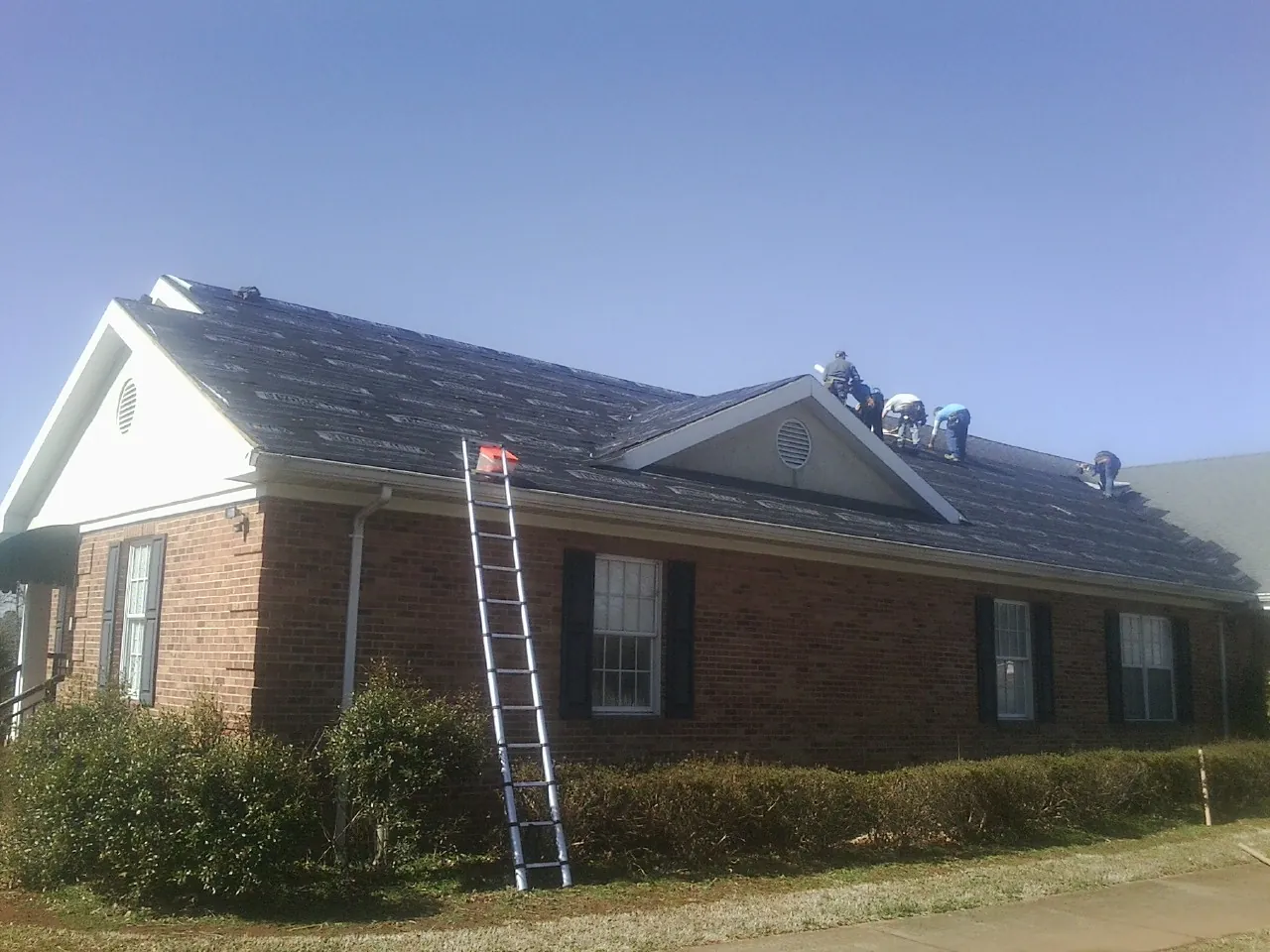 Crew tearing shingles off a brick ranch roof with a ladder set — Emergency Roof Repair work by our crew in Buffalo Grove
