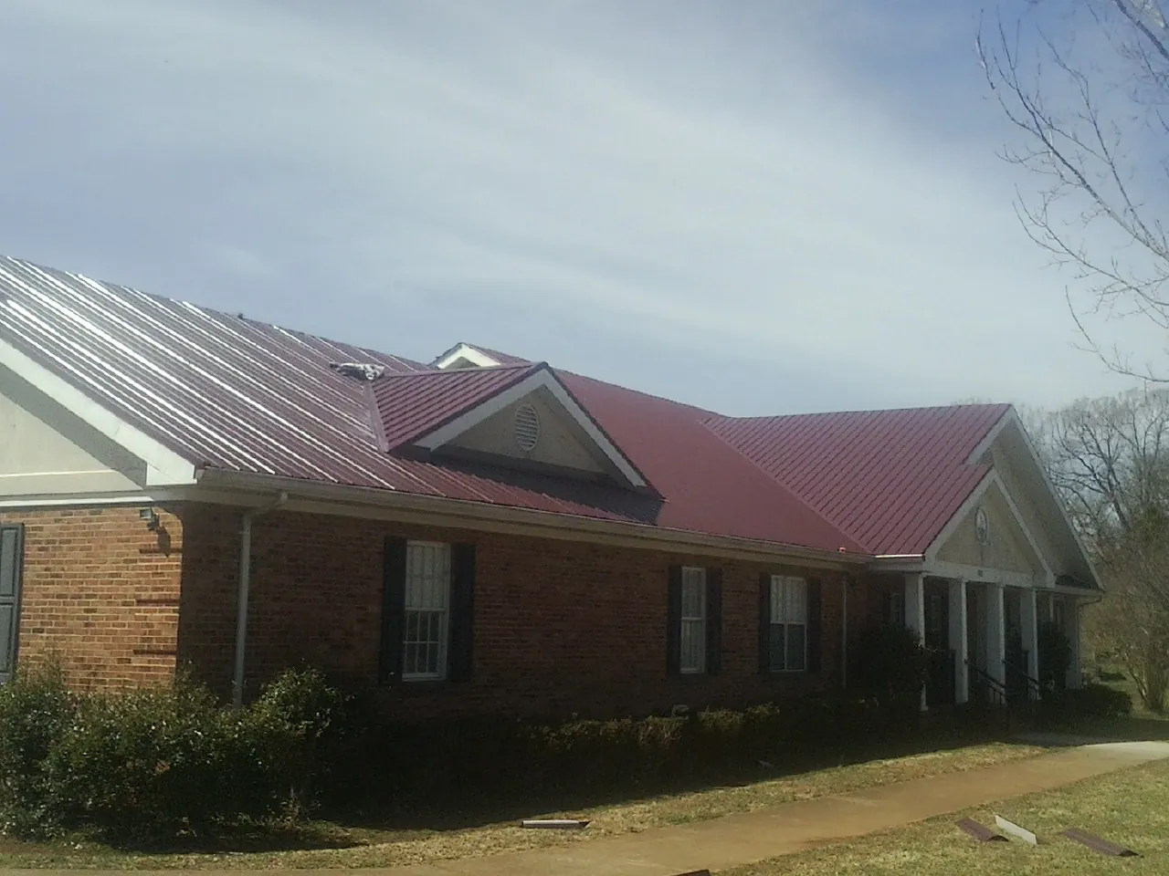 Red metal roof with gabled entries on a long brick building, from a Hail Damage Roof Repair job in Buffalo Grove