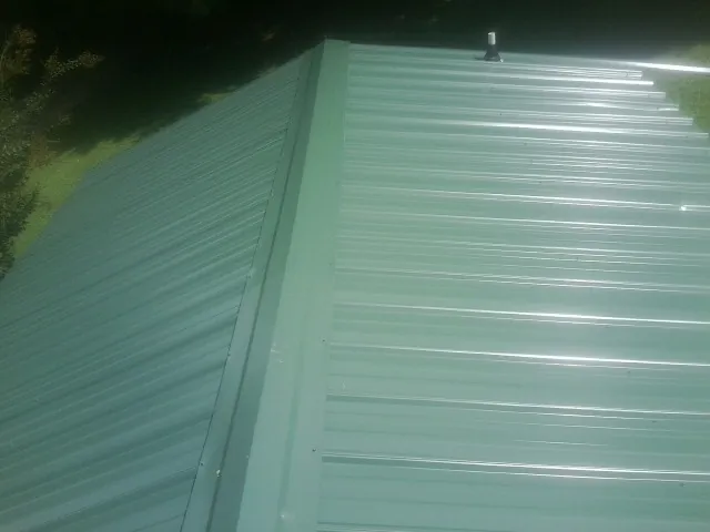 New green metal panels meeting at the ridge of a roof — Flat Roof Repair work by our crew in Buffalo Grove