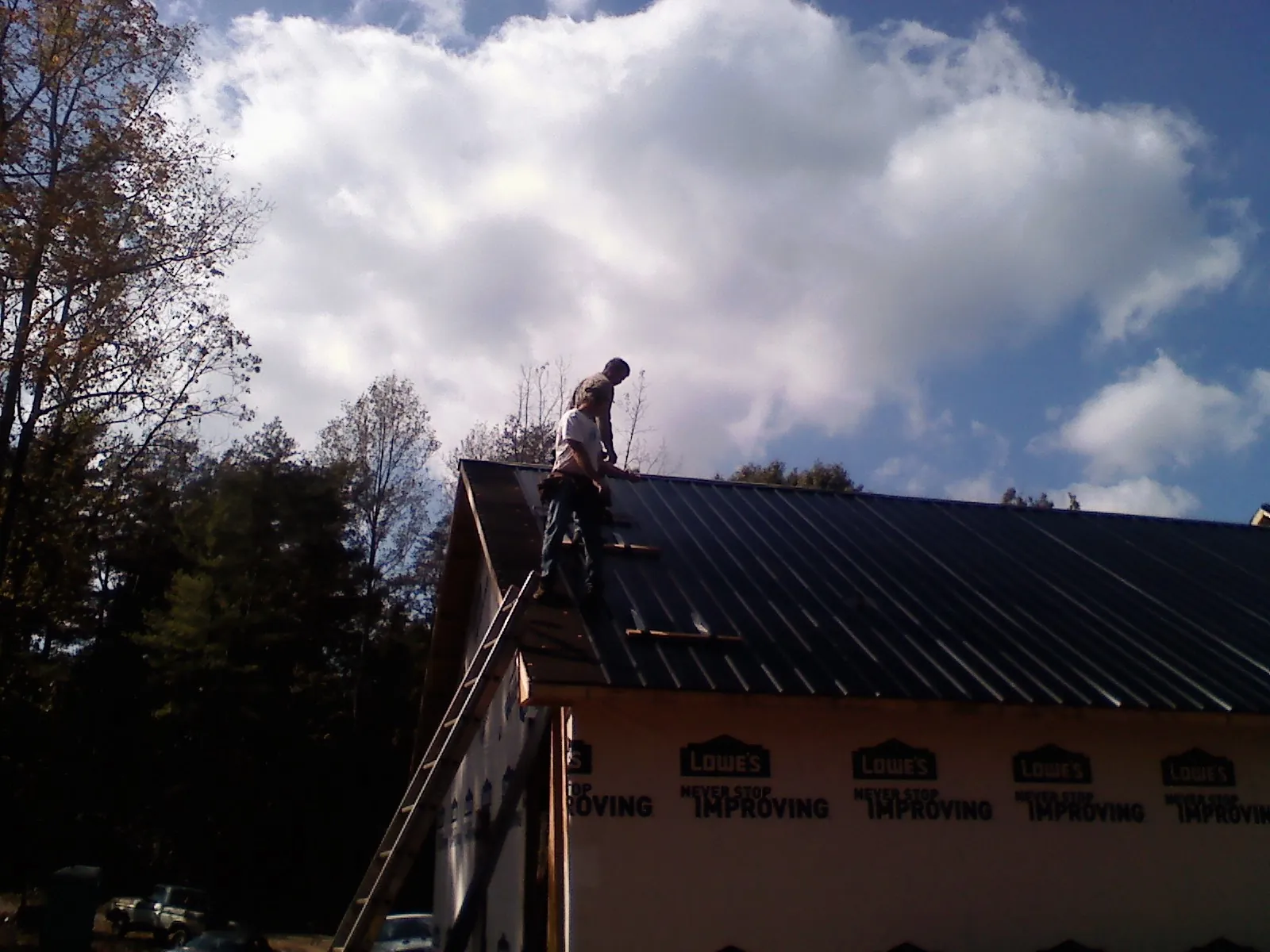 Roofer fastening dark metal panels high against a cloudy sky, from a Roof Inspection job in Buffalo Grove
