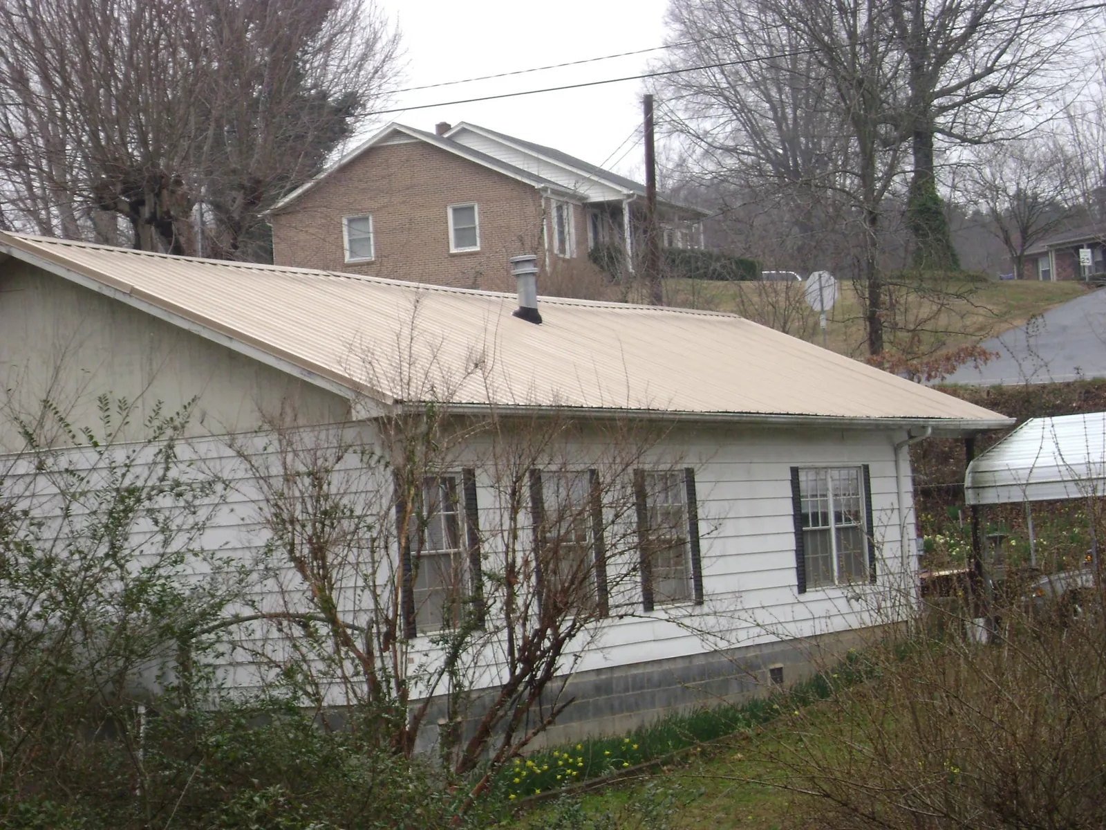 Tan metal roof on a white sided house set into a hillside — Commercial Roofing by Roofing Brothers in Buffalo Grove